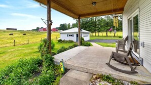 A covered porch with a concrete floor, a rocking chair, and a small garden area with a decorative post.