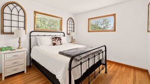 A bedroom with a bed, bedside tables, a dresser, and two windows with blinds.