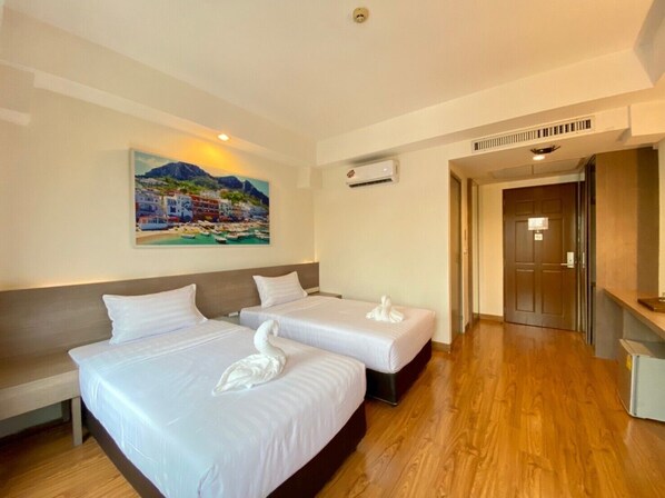 Habitación de hotel con dos camas, un cuadro de una escena costera, un equipo de aire acondicionado y piso de madera.