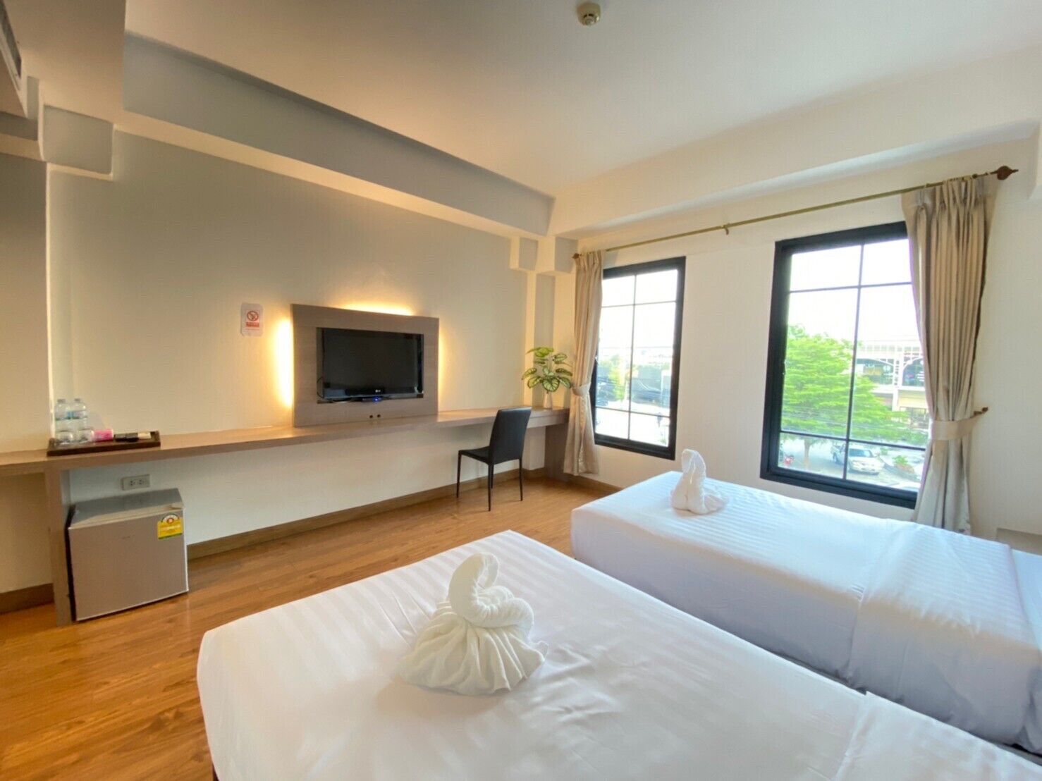 A hotel room with two beds, a TV mounted on the wall, a desk, a chair, and a window with curtains.