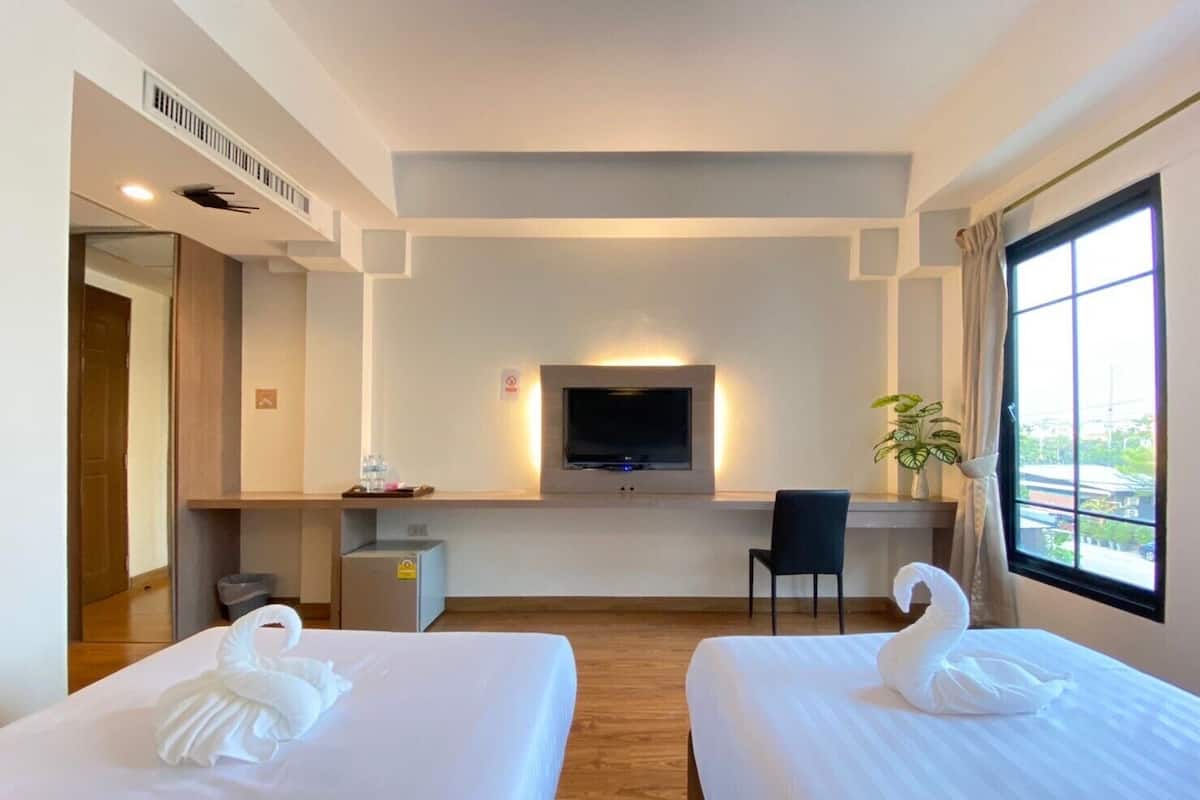Quarto de hotel com duas camas, televisão, secretária e janela.