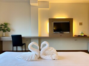 Habitación de hotel con cama, escritorio, silla, televisor y planta.