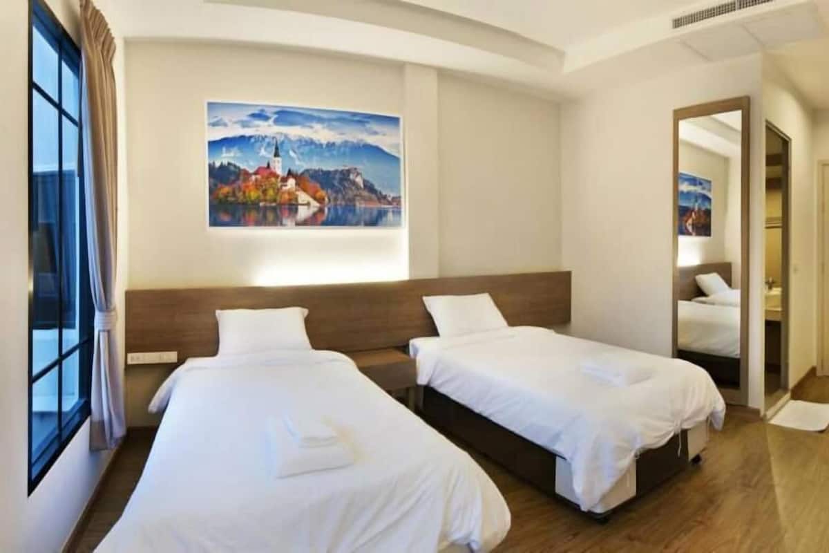 Quarto de hotel com duas camas, um quadro na parede e uma porta que dá para o banheiro.