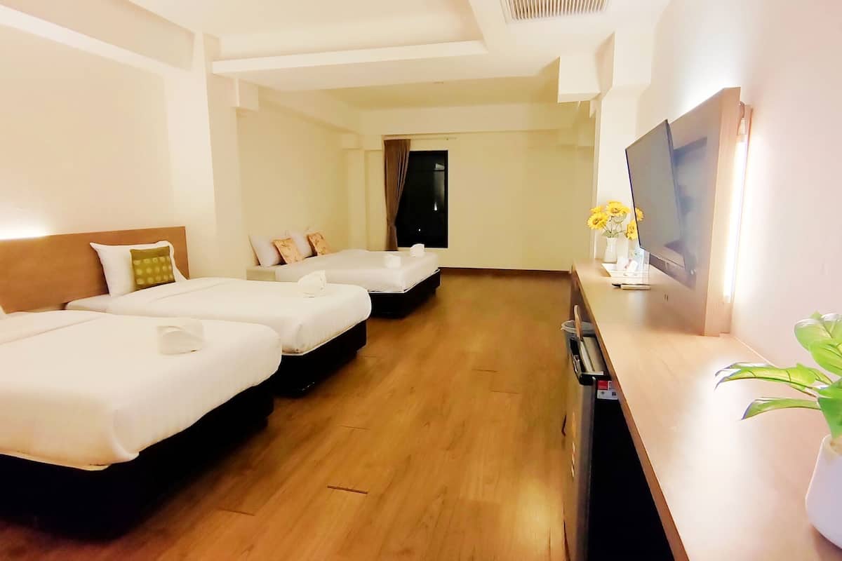 Quarto de hotel com três camas, televisão de tela plana, planta em vaso e piso de madeira.