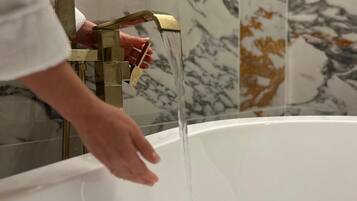 Eine Hand dreht einen Messing-Wasserhahn, während Wasser in eine weiße Badewanne fließt.