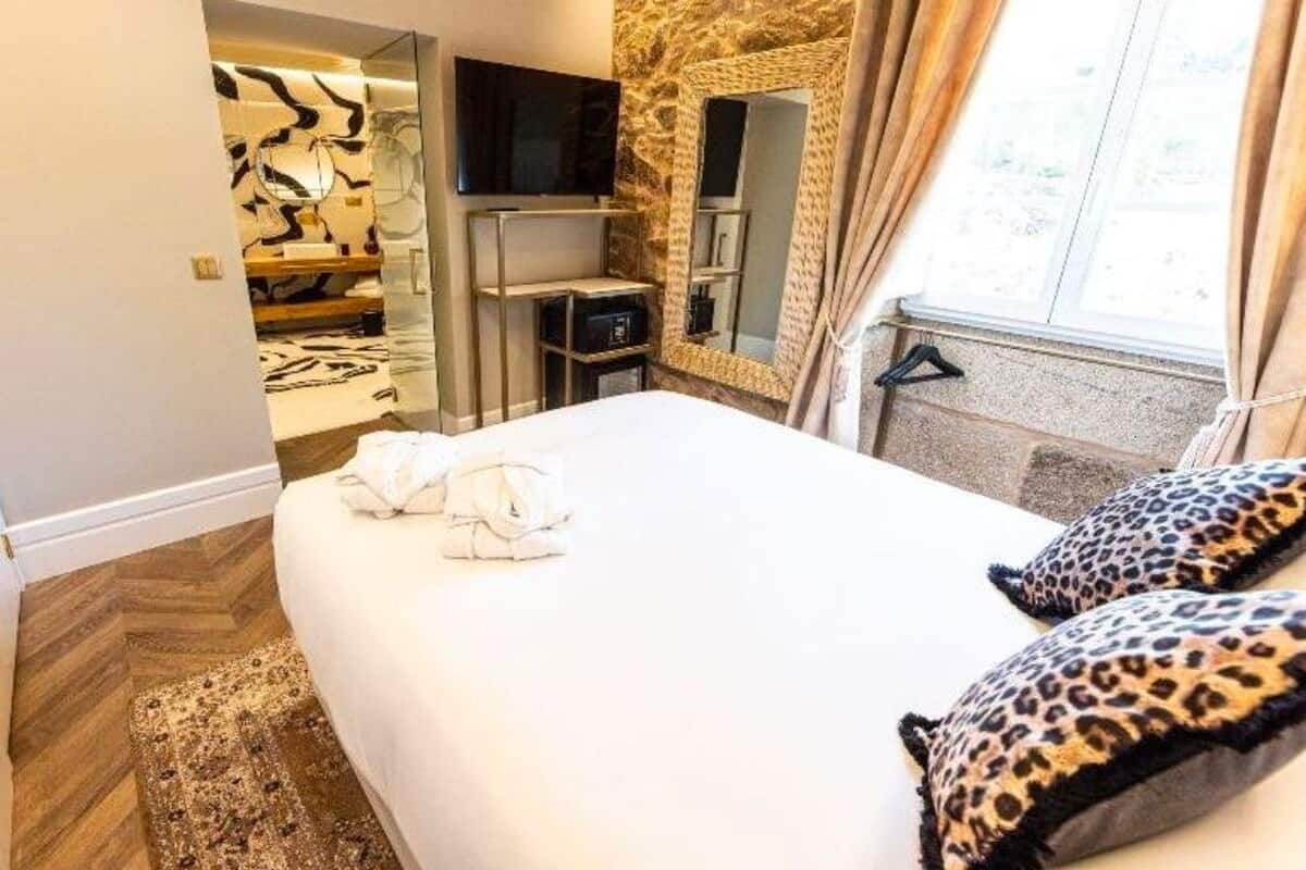 Una habitación de hotel con cama, televisor, espejo y pared de piedra.