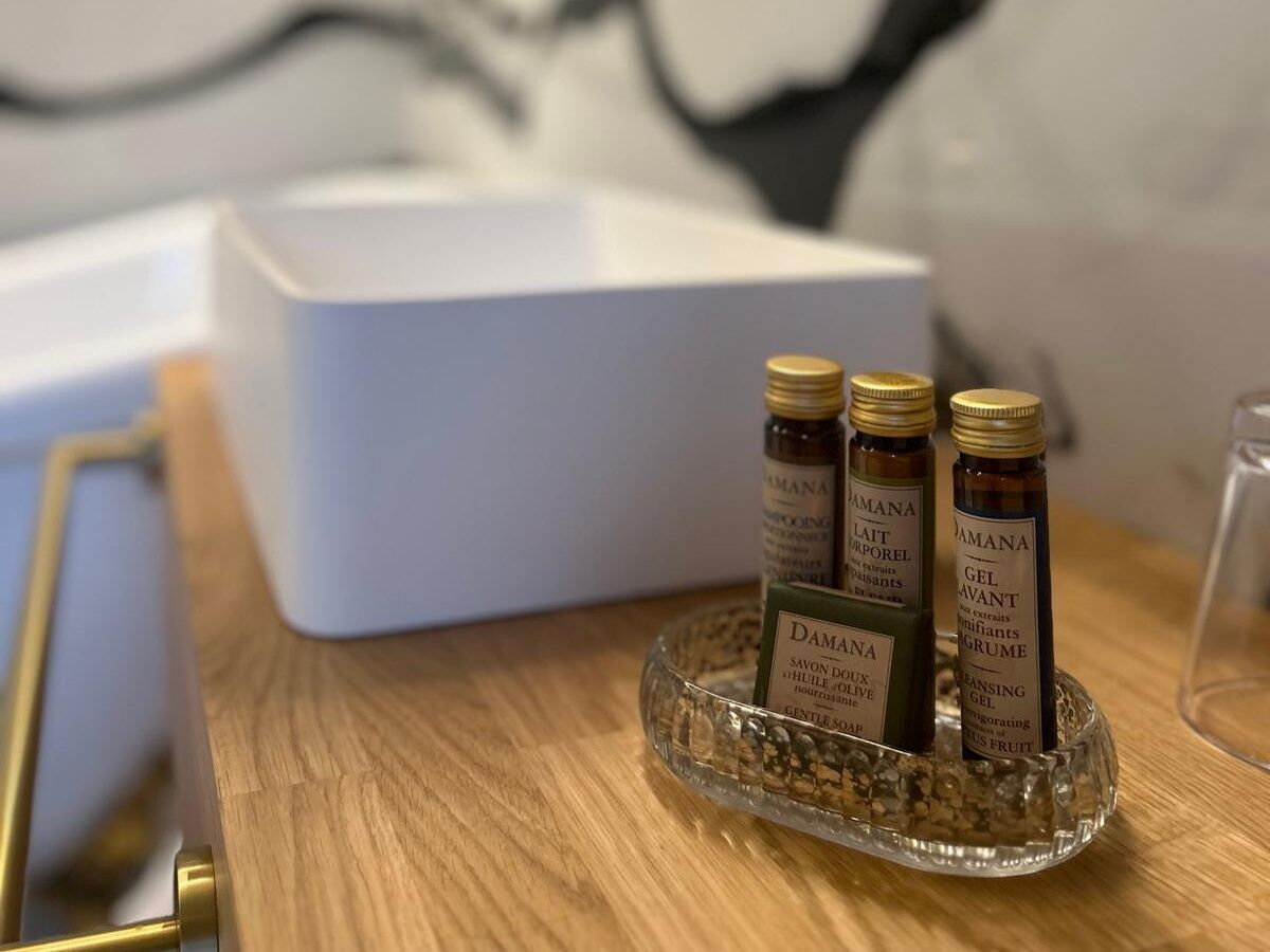 Una mesa de madera con tres botellas de productos Damana, una caja blanca y un recipiente de vidrio.