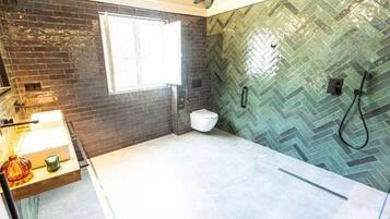 Un baño con pared de diseño en patrón de espiga, una ventana, un inodoro y zona de ducha.