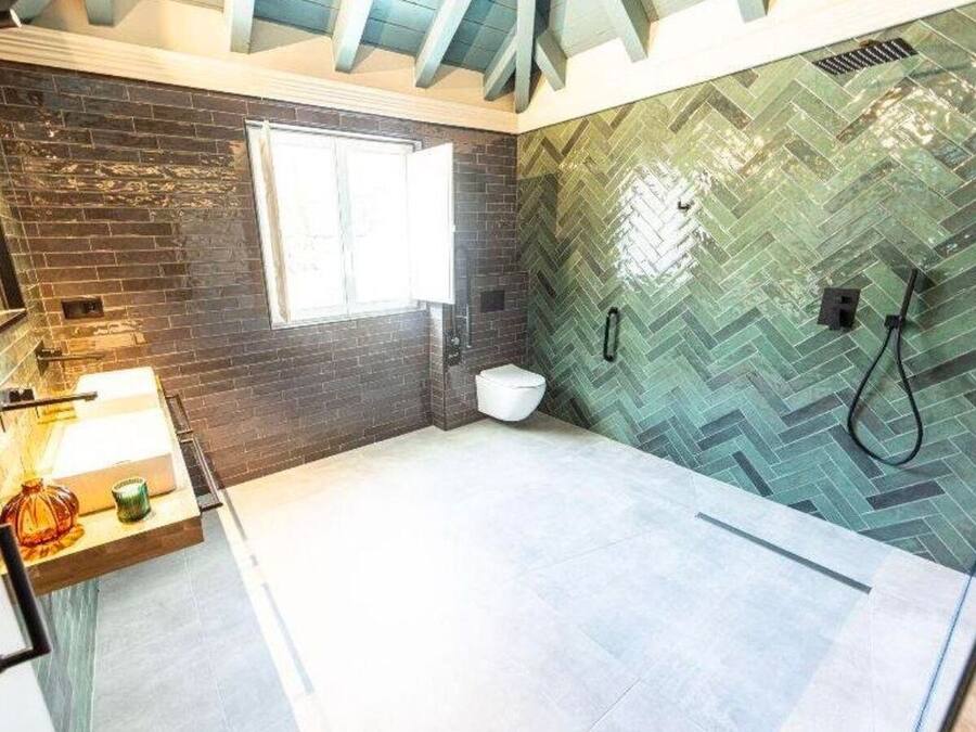 Un baño con pared de diseño en patrón de espiga, una ventana, un inodoro y zona de ducha.