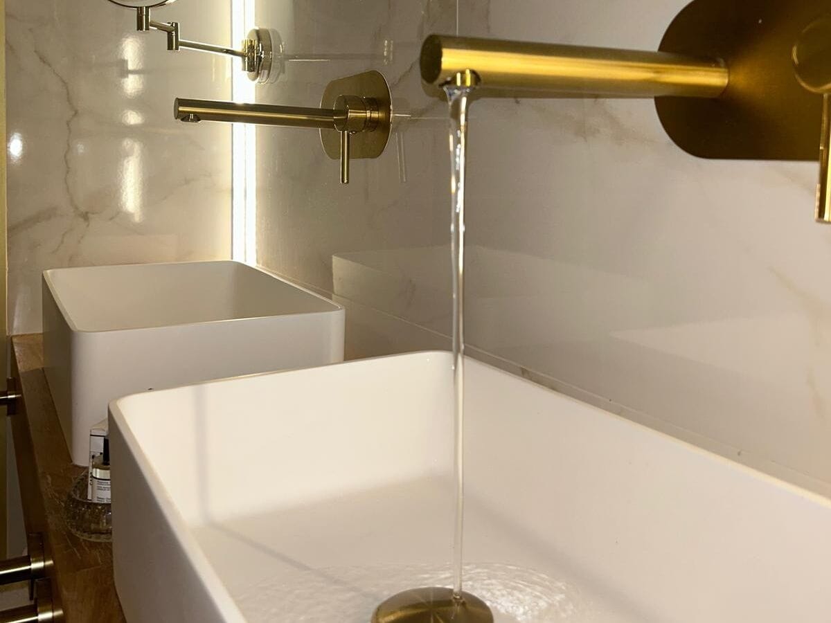 Et moderne badeværelse med et hvidt badekar, en guldfarvet hane og et hvidt konsolbord.