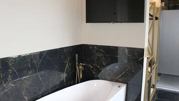 A modern bathroom with a freestanding bathtub, marble walls, and a mounted television.