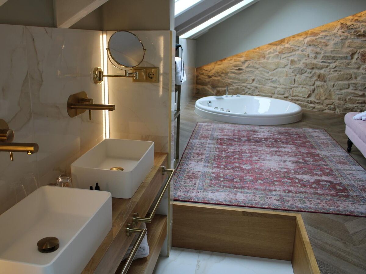A modern bathroom with a freestanding bathtub, two sinks, a mirror, and a stone wall.