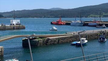 Un puerto con barcos amarrados, un muelle de piedra y una vista despejada del agua y colinas lejanas.