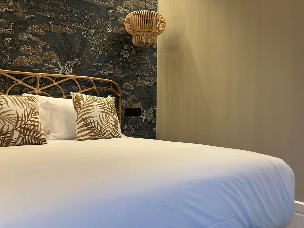 Una cama con ropa blanca, un cabecero tejido y almohadas estampadas.