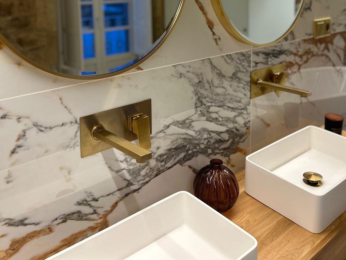 Un baño con paredes de mármol, un grifo dorado y un espejo.