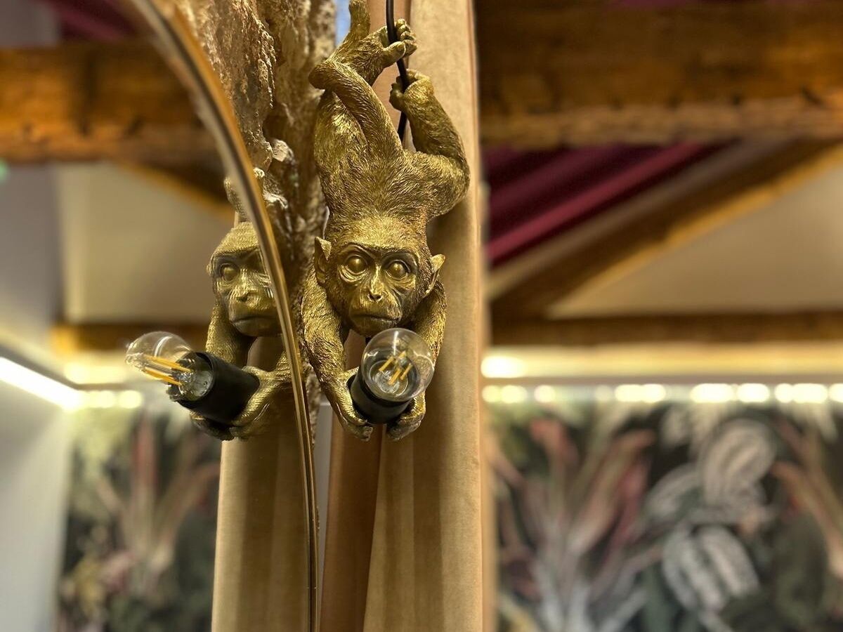 Een decoratieve messing lampfitting met een aapfiguur die een gloeilamp vasthoudt.