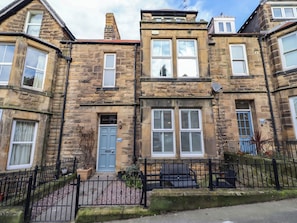 A stone-built townhouse with a blue front door, multiple windows, and a black metal fence.