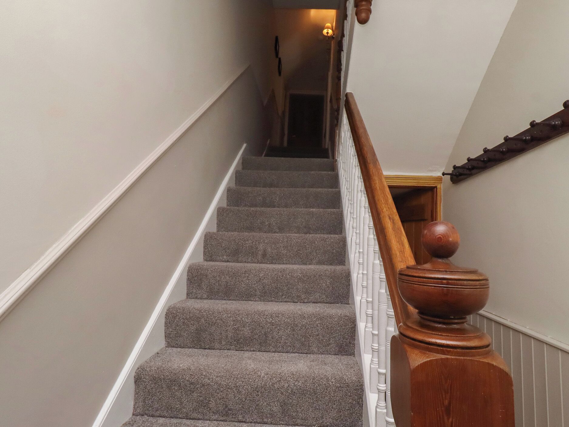 A carpeted staircase with a wooden handrail and a white banister.