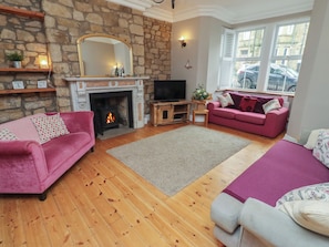 A cozy living room with a stone fireplace, a flat-screen TV, and two pink sofas.