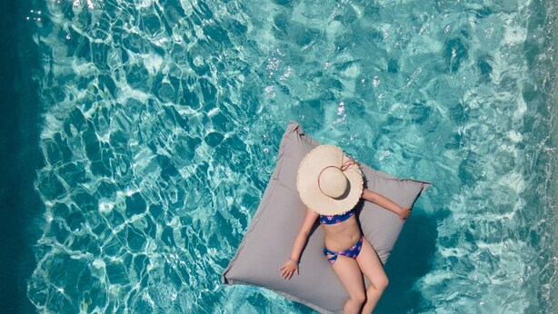 Una persona estesa sobre una plataforma flotant a una piscina de blau clar.