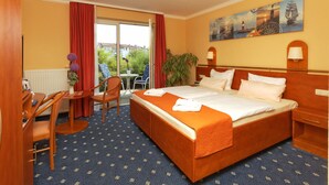 Een hotelkamer met een groot bed, een bureau met stoel, een kleine tafel met stoel, en uitzicht op het omliggende landschap door een schuifdeur.