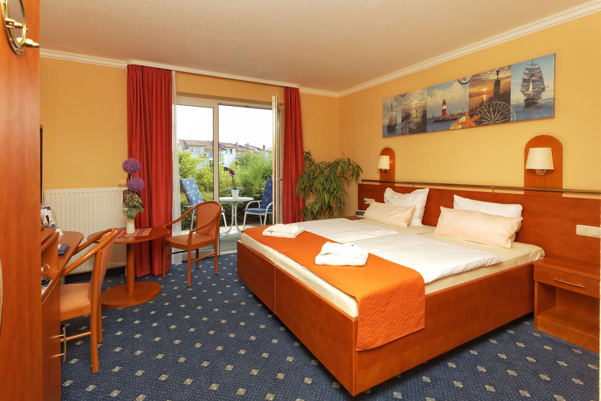 Een hotelkamer met een groot bed, een bureau met stoel, een kleine tafel met stoel, en uitzicht op het omliggende landschap door een schuifdeur.