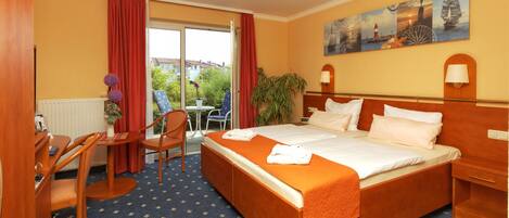 Habitación de hotel con una cama grande, un escritorio con silla, una mesita con otra silla, y vistas al exterior a través de una puerta corredera.