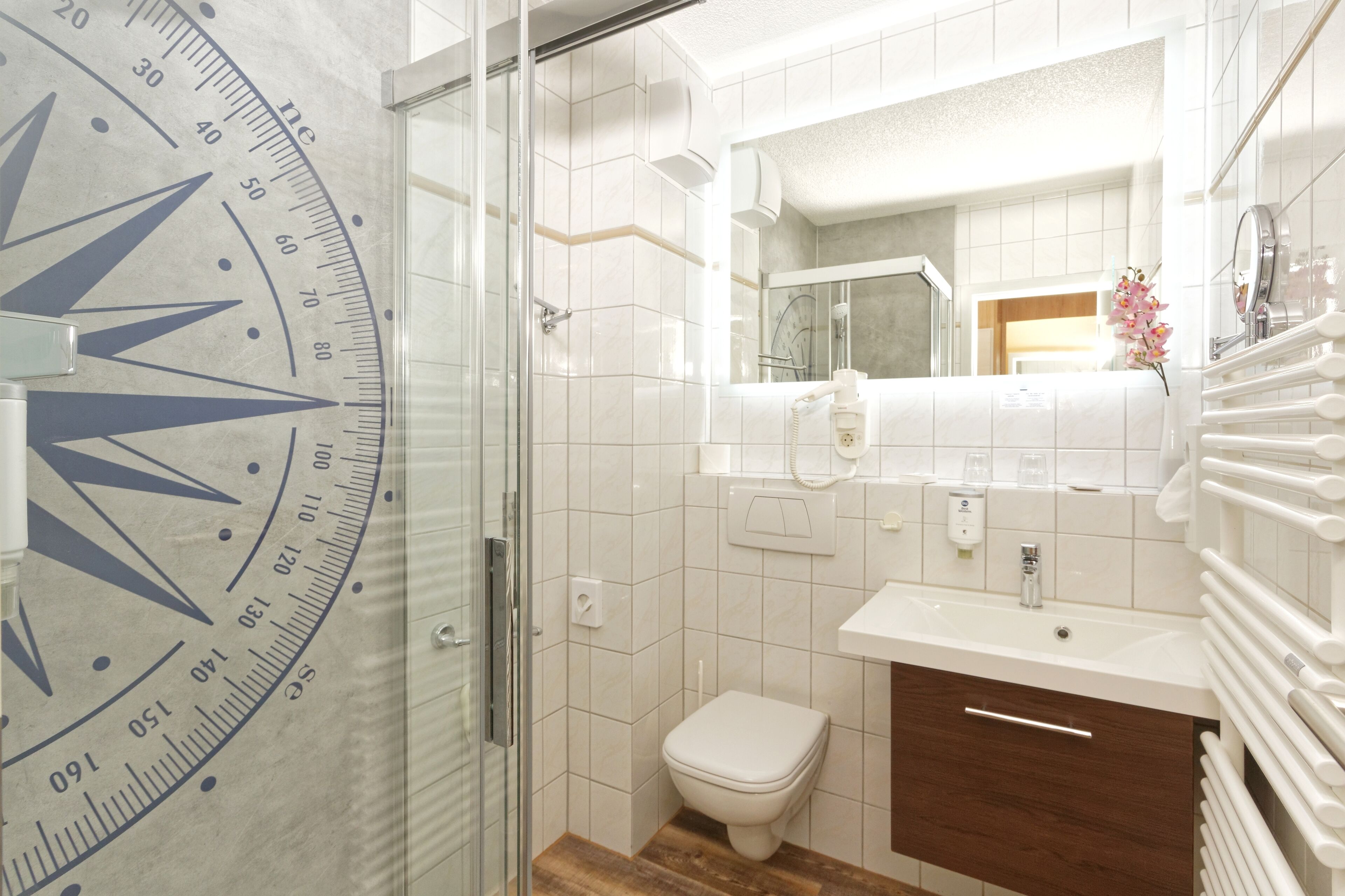 A bathroom with a compass design on the wall, a toilet, a sink, and a shower area.