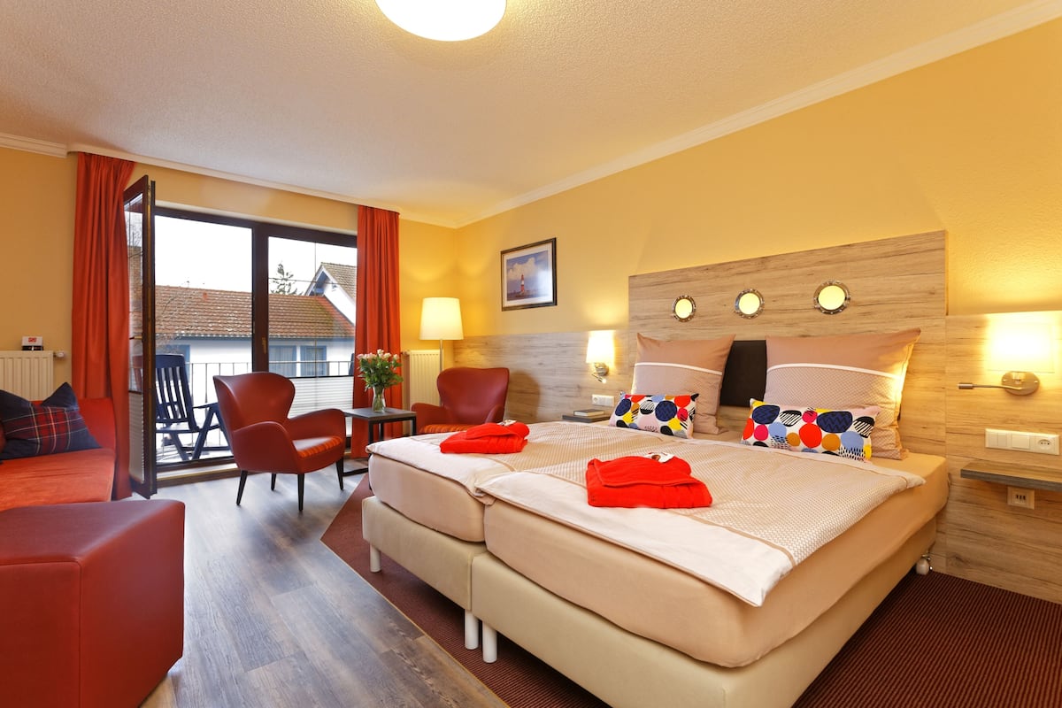 Een hotelkamer met een tweepersoonsbed, twee stoelen, een kleine tafel, een lamp en een raam met gordijnen.