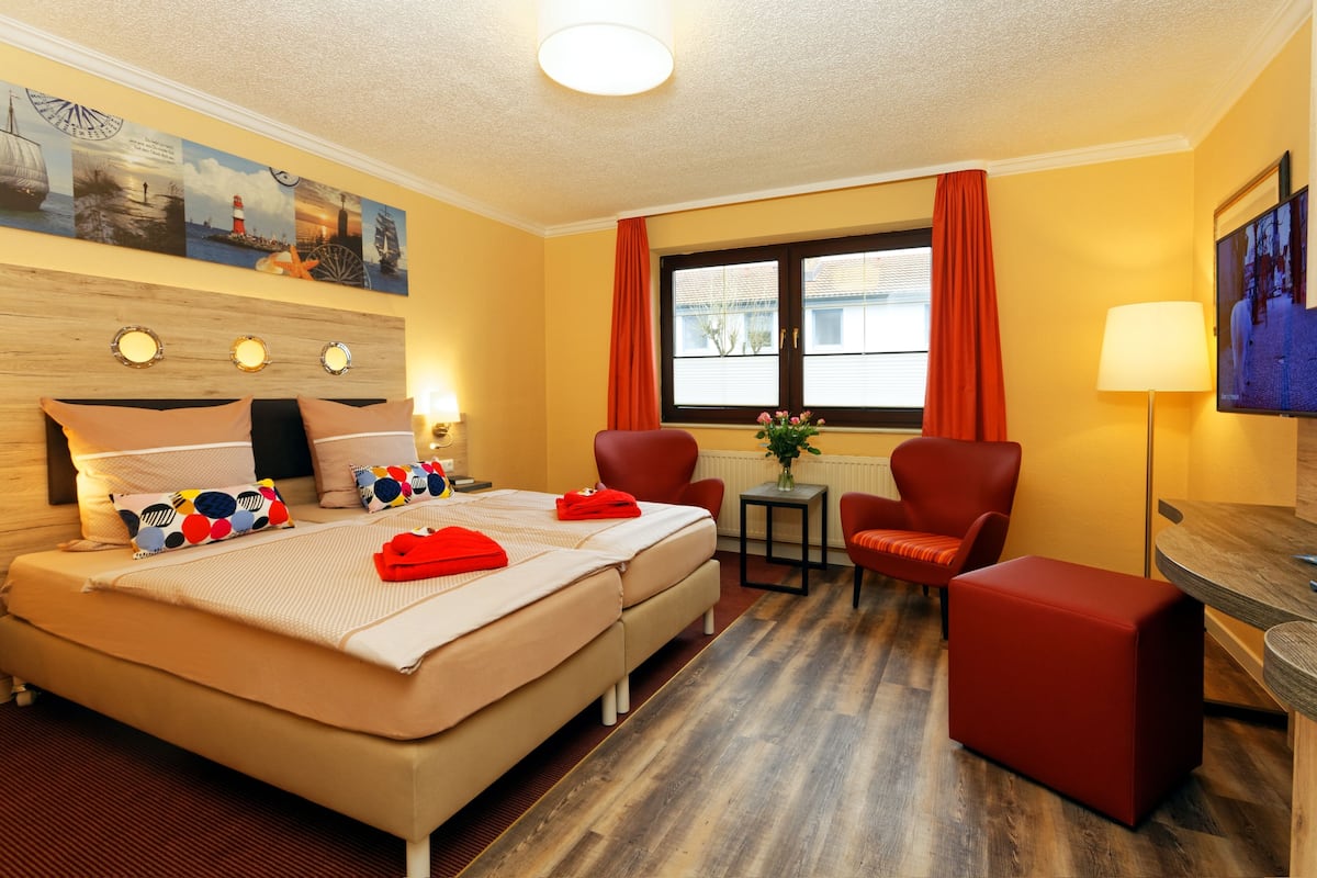 Een hotelkamer met een bed, twee stoelen, een kleine tafel, een televisie en een raam met gordijnen.