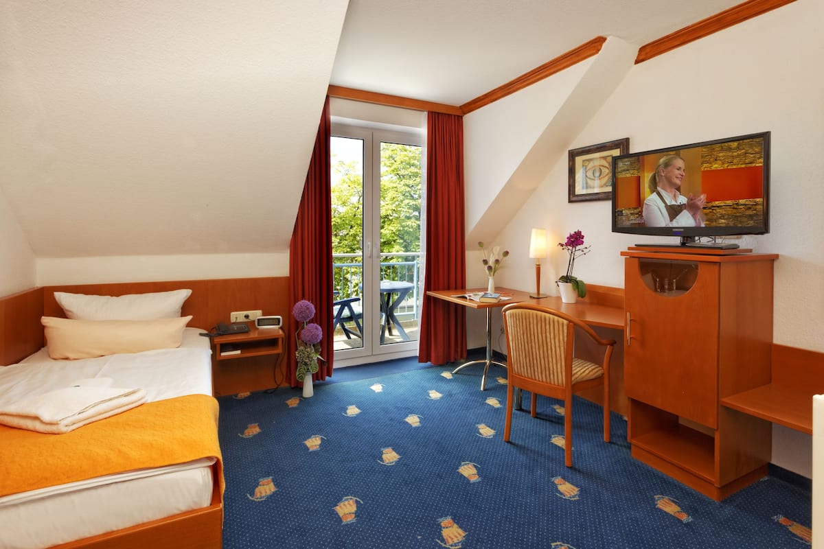 Hotelkamer met een bed, een bureau, een stoel, een televisie en een balkon met rode gordijnen.