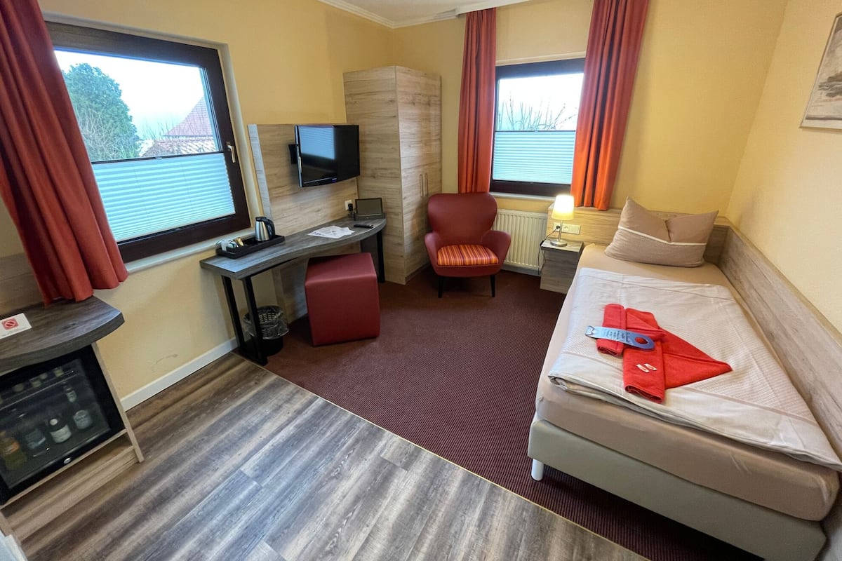 Een hotelkamer met een bed, bureau, stoel, televisie en ramen met gordijnen.