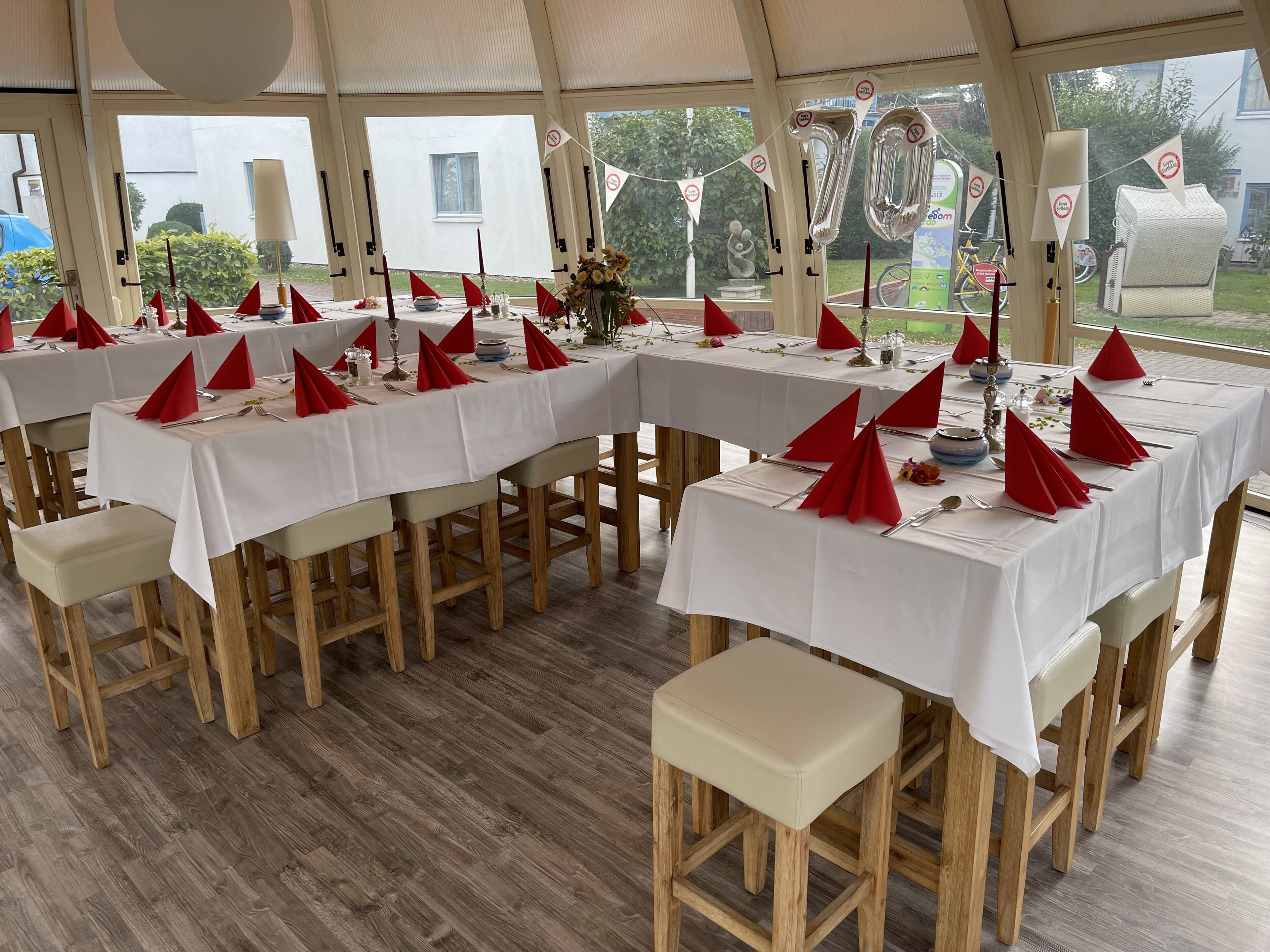 Een overdekte eethoek met gedekte tafels voor een maaltijd, met rode servetten en witte tafellakens.