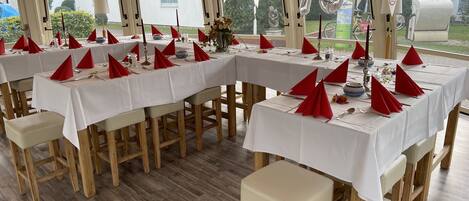 Een overdekte eethoek met gedekte tafels voor een maaltijd, met rode servetten en witte tafellakens.