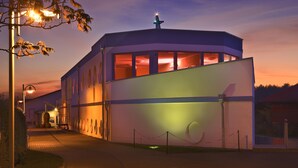 Een modern gebouw met een golvend dak en grote ramen, omringd door een hek van gaas.