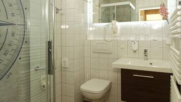 Un baño con cabina de ducha de vidrio, inodoro blanco, suelo de madera, lavabo blanco y mueble de madera oscura.
