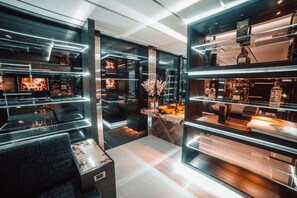 Un espace bar moderne avec des étagères en verre où sont exposées les bouteilles, et un coin salon central avec une table et des chaises en marbre.