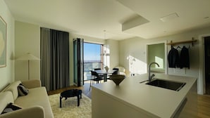 Quarto de hotel moderno com área de refeições, uma janela grande com vista para a cidade, um sofá e um cão pequeno.