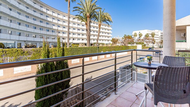 Un balcon d’hôtel avec des sièges d’extérieur, des palmiers et une vue sur un bâtiment moderne.