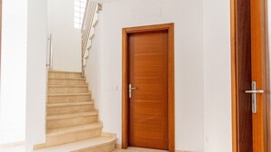 Un escalier menant à une porte en bois dans une pièce aux murs blancs et au sol carrelé.