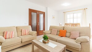 Un salon avec deux canapés beige, une table basse en bois et une porte en bois dotée de panneaux de verre.