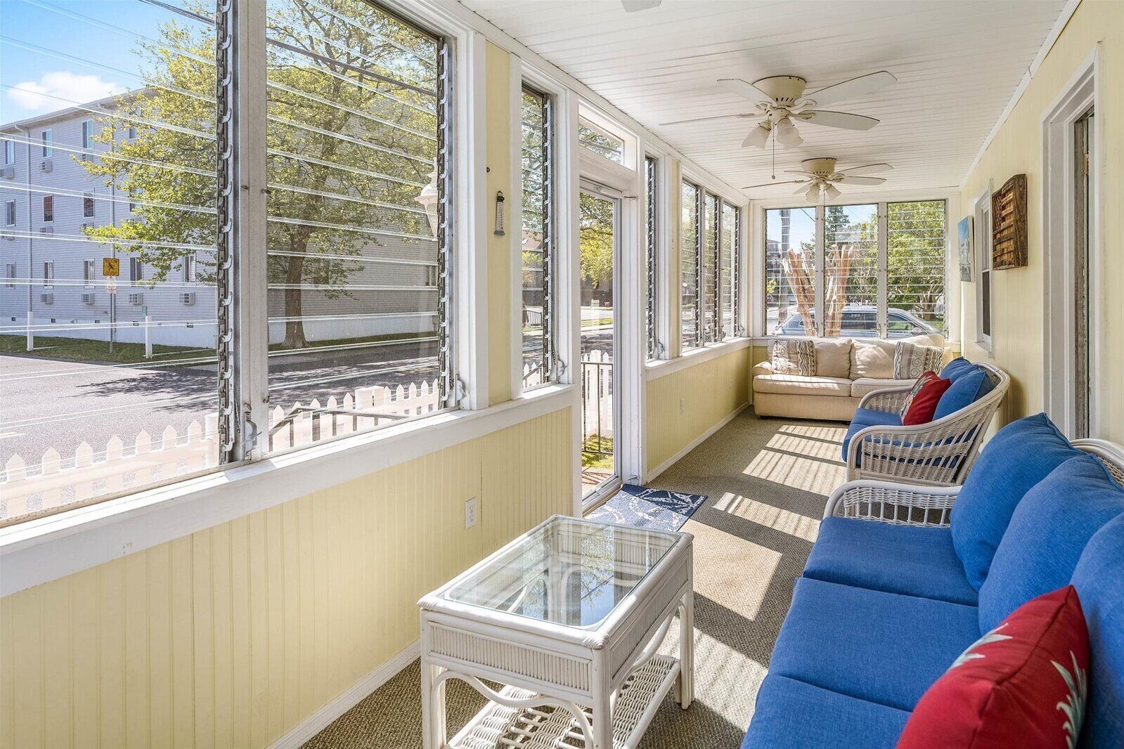 Eine überdachte Veranda mit einem blauen Sofa, einem Glastisch und einem Deckenventilator.