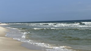 Uma praia com pegadas na areia e ondas se aproximando da costa.