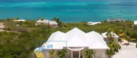 Edifício branco com cúpula, rodeado por vegetação e vista para o oceano.