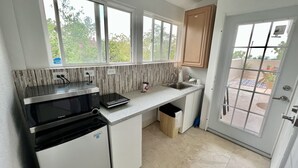 Une cuisine moderne équipée d’un four à micro-ondes encastré, d’un petit évier et d’une fenêtre donnant sur un jardin.