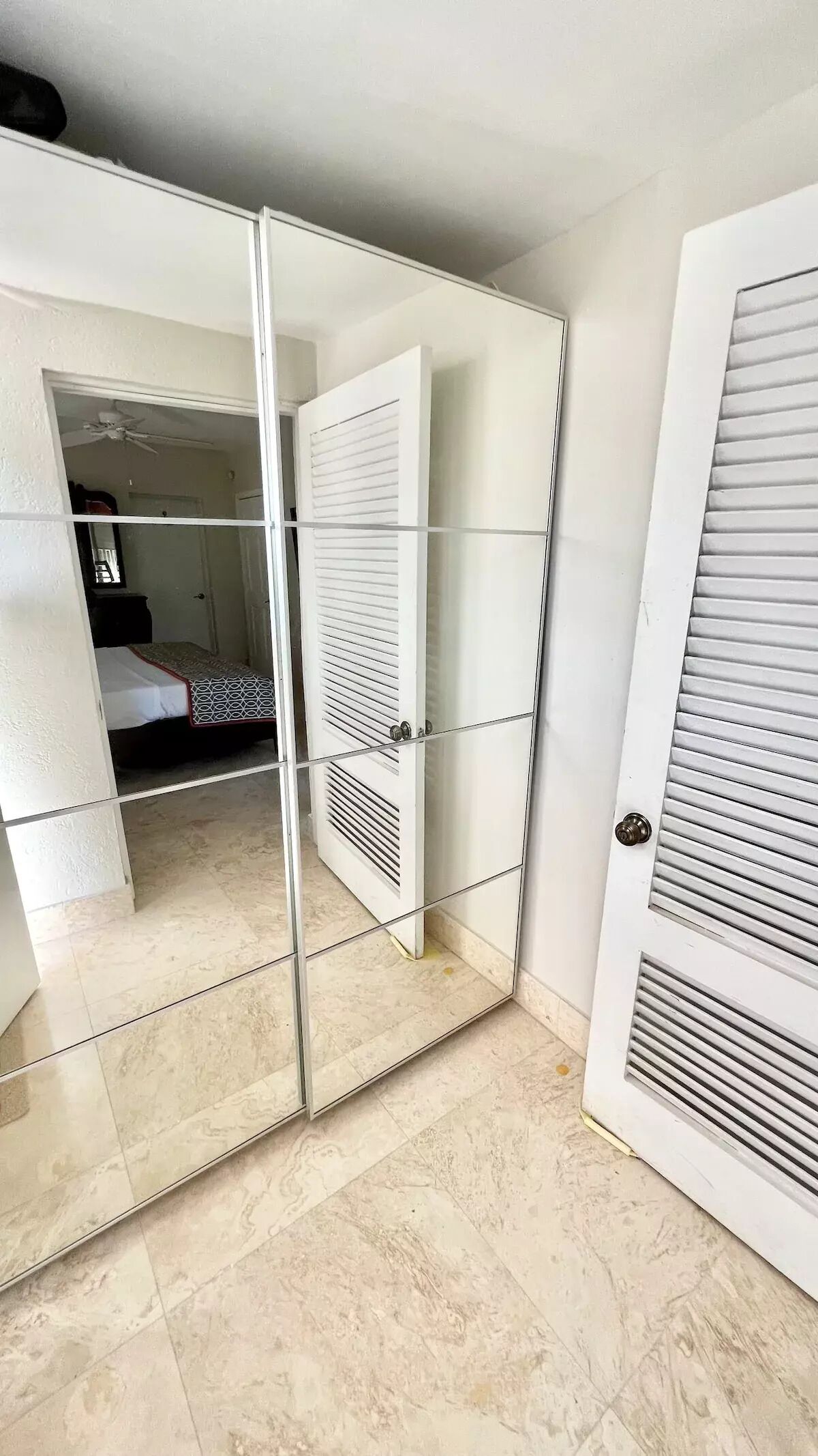 A room with a mirrored wardrobe, a bed with a patterned bedspread, and a ceiling fan.