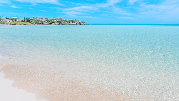 Une plage dégagée, avec une mer calme et une côte lointaine parsemée de bâtiments.