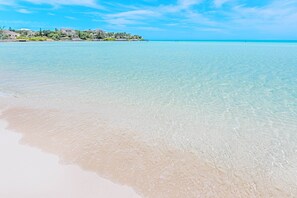 Une plage dégagée, avec une mer calme et une côte lointaine parsemée de bâtiments.