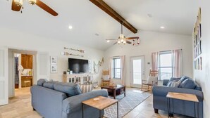 A spacious living room with a large sofa, a smaller sofa, and a coffee table. There is a television mounted on the wall, a ceiling fan, and a fireplace.