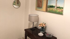 Une pièce avec une table en bois foncé, une lampe, un vase de fleurs et un mur orné d’un tableau et de deux miroirs.
